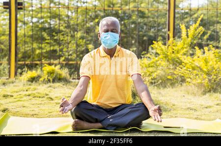 Homme senior dans le masque médical méditant sur le tapis de yoga au parc - concept des personnes âgées soins de santé, forme physique pendant la pandémie de coronavirus covid-19 Banque D'Images