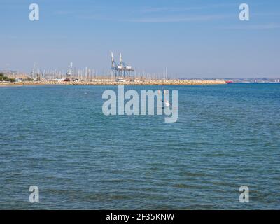 Vue depuis la jetée sur l'homme pagayant en canoë et les personnes nageant dans la mer méditerranée à Larnaca, Chypre. Grues et yachts à l'horizon. Banque D'Images