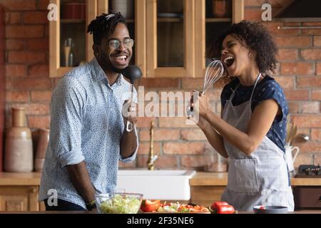 Un jeune couple africain chante une chanson dans des microphones d'ustensiles de cuisine Banque D'Images