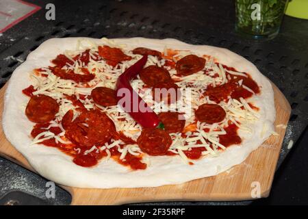 Pizza Pepperoni maison à la guesy avant de faire cuire sur une planche à pizza en bois Banque D'Images