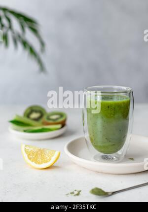 smoothie vert coloré avec épinards, céleri, kiwi, citron et poudre de super-nourriture verte dans un verre à double paroi. nourriture végétalienne. fond gris avec vert Banque D'Images