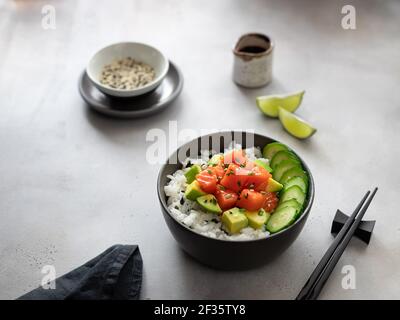 Poke Bowl servi avec du saumon, de l'avocat, du concombre et du riz sur fond gris. Bol Bouddha. Vue latérale. Emplacement pour le texte. Banque D'Images