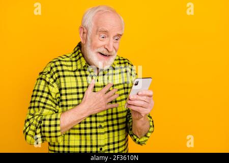 Photo de drôles grand-père tenir téléphone regarder écran main poitrine porter une chemise à carreaux vert isolée jaune sur fond Banque D'Images