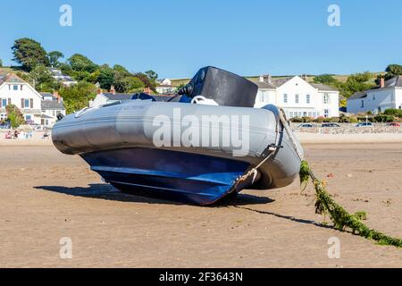 Un grand canot pneumatique en caoutchouc situé sur son côté sur la plage à marée basse, sa corde d'amarrage festoonée d'algues, Instaw, Devon, Royaume-Uni Banque D'Images