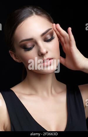 Portrait de beauté de la jeune femme avec la main près du visage sur fond noir. Brunette fille avec maquillage de soirée et noir dess touche le visage avec le toitures Banque D'Images