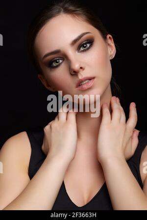 Portrait de beauté de la jeune femme aux yeux verts avec la main près du visage sur fond noir. Brunette fille avec maquillage de soirée et noir dess touche nec Banque D'Images