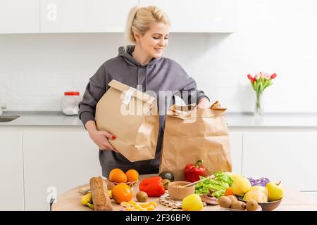 La femme règle les achats dans la cuisine. Livraison de produits d'épicerie dans des sacs en papier. Service d'abonnement de l'épicerie dans des conditions de quarantaine parce que Banque D'Images