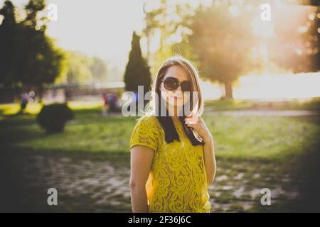 Belle fille souriante avec des cheveux foncés dans un chemisier jaune en position de stationnement Banque D'Images