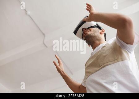 Vue très basse sur un jeune homme en utilisant la VR et en allant contre un plafond blanc, espace de copie Banque D'Images