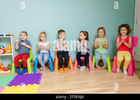 Les enfants sont assis sur les chaises colorées, claquant la main Banque D'Images