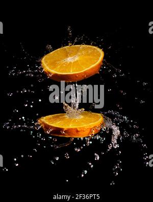 image de composition créative de tranches d'orange juteuses qui tournent et éclabousse eau isolée sur fond noir Banque D'Images