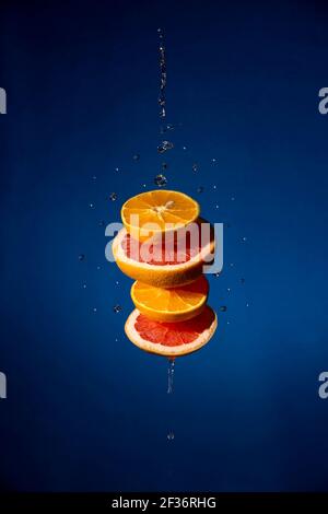tranches d'orange et de pamplemousse lévitant avec des gouttes d'eau sur texture arrière-plan bleu Banque D'Images