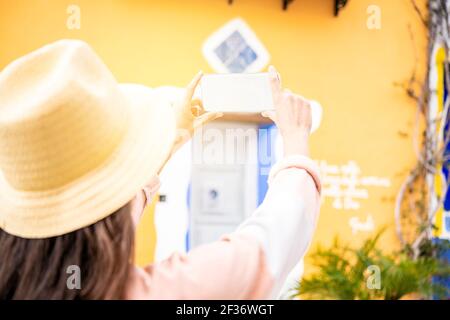 Vue de derrière une jeune femme touristique solo avec prise de chapeau photo avec maquette de smartphone Banque D'Images