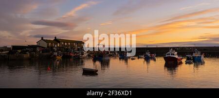 Lyme Regis, Dorset, Royaume-Uni. 15 mars 2021. Météo au Royaume-Uni: Le ciel du soir au-dessus du port de Cobb à Lyme Regis brille de couleur dorée chaude au coucher du soleil avant les prévisions météorologiques plus chaudes cette semaine. Credit: Celia McMahon/Alamy Live News Banque D'Images