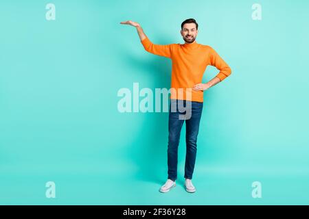 Pleine photo de jeune beau homme souriant positif mesure taille hauteur porter un chandail orange isolé sur fond de couleur sarcelle Banque D'Images