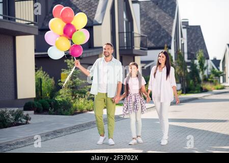 Photo pleine grandeur de joyeux souriant gai positif bon ambiance famille marcher à l'extérieur tenir ballons célébrer anniversaire Banque D'Images