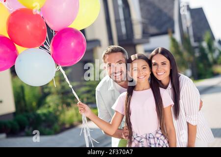 Photo de famille positive souriante à l'extérieur maman papa célébrez l'anniversaire de votre fille, une fille tient des ballons Banque D'Images