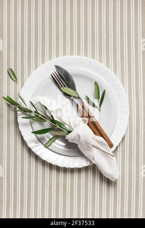 Table festive avec assiette blanche, couverts et décoration avec branches d'olive. Beau plan de pose. Banque D'Images