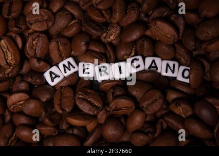 Gros plan de grains de café fraîchement torréfiés près du mot AMERICANO écrit avec de petits cubes blancs. Vue du dessus. Banque D'Images