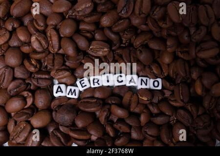 Gros plan de grains de café fraîchement torréfiés près du mot AMERICANO écrit avec de petits cubes blancs. Vue du dessus. Banque D'Images