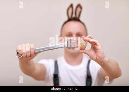 Vacances de Pâques, concept de célébration. Travailleur ou mécanicien souriant drôle porte des oreilles de lapin sur la tête, tenant des clés et peint blanc d'oeuf Banque D'Images