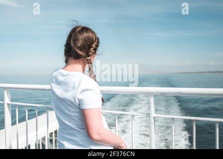 Jeune jolie fille au soleil sur le pont de bateau regardant sortie en mer à l'écart du port bleu été ciel Banque D'Images