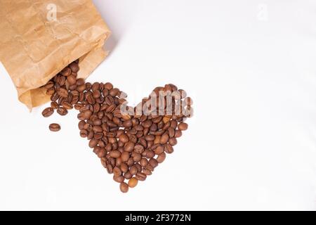 Grains de café fraîchement torréfiés en forme de coeur près d'un sac de papier isolé sur fond blanc. Vue du dessus. Banque D'Images