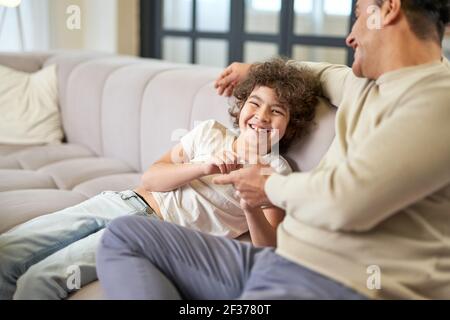 Des moments de plaisir. Joyeux garçon latin s'amusant tout en passant du temps avec son père, jouant dans le salon à la maison Banque D'Images