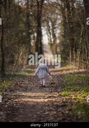 Une photo verticale d'une petite fille marchant sur un chemin avec un ours en peluche dans sa main Banque D'Images