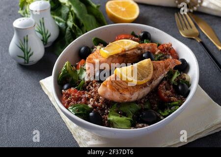 Dans une assiette de quinoa, saumon, épinards, olives noires, citron et tomates cerises sur fond gris. Une alimentation saine. Banque D'Images