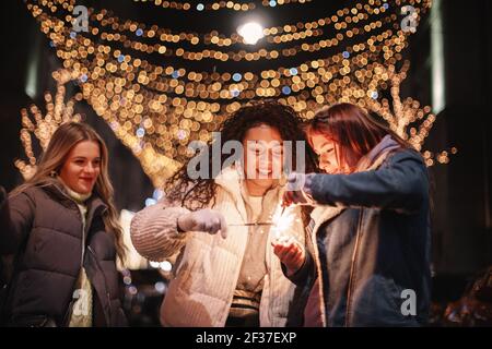 Amies féminines heureuses allumant des pétillants en ville pendant noël Banque D'Images