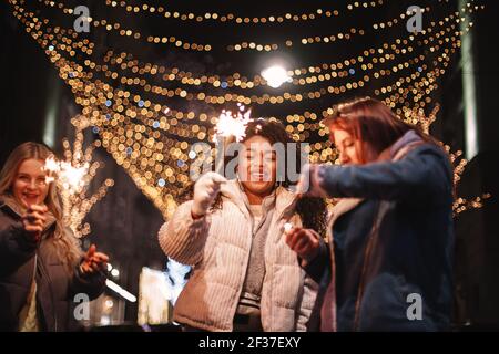 De jeunes femmes heureuses tenant des spamisseurs debout en ville pendant Noël Banque D'Images