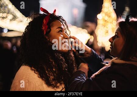 Heureuse jeune femme debout avec petite amie en ville pendant noël Banque D'Images