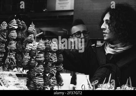 Les jeunes hommes achètent des brochettes de fraises fraîches enrobées de chocolat de la boîte aux fruits du célèbre marché alimentaire de Barcelone la Boqueria. Barcelone, Espagne. Noir blanc Banque D'Images