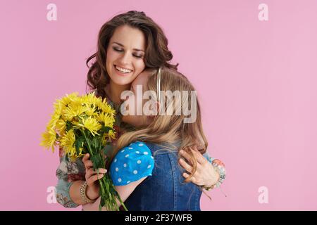 une mère et un enfant souriants et élégants, avec de longs cheveux ondulés et des fleurs de chrysanthèmes jaunes sur fond rose. Banque D'Images