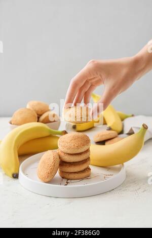 Main féminine avec de savoureux biscuits à la banane sur fond clair Banque D'Images