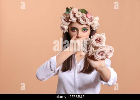 Portrait d'une belle jeune femme avec maquillage créatif et fleurs sur fond de couleur Banque D'Images