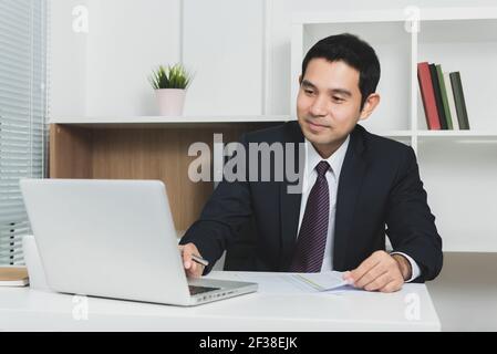 Beau homme d'affaires asiatique utilisant un ordinateur portable dans le bureau - ton doux, foyer sélectif Banque D'Images