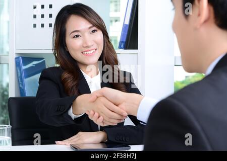Femme d'affaires asiatique se faisant poignée de main avec un homme d'affaires dans le bureau Banque D'Images