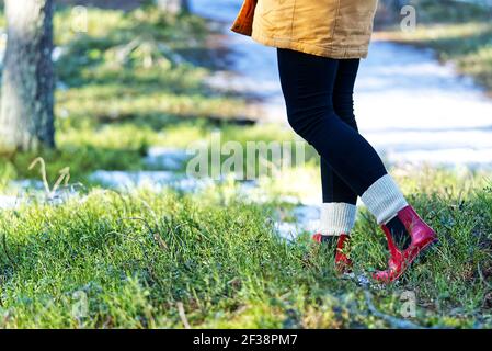 Concept automne ou printemps avec forêt colorée et bottes de pluie à l'extérieur. Gros plan des pieds de femme marchant dans des bottes rouges. Banque D'Images