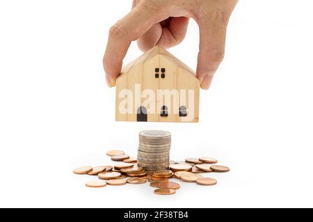 La main d'une femme tient une maison en bois modèle sur une pile de pièces sur fond blanc. Banque D'Images