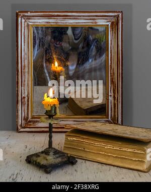 Une bougie allumée se reflète dans un vieux miroir dans un cadre en bois et illumine les livres sur la table. Vintage. Banque D'Images