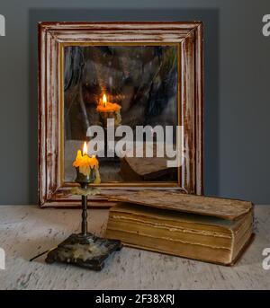 Une bougie allumée se reflète dans un vieux miroir dans un cadre en bois et illumine les livres sur la table. Vintage. Banque D'Images