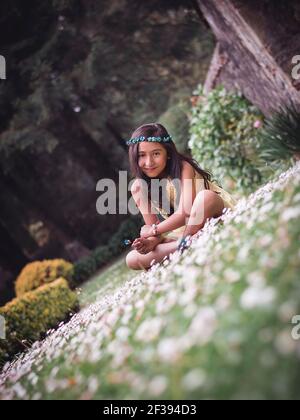 Adolescente assise sur l'herbe dans un parc portant une robe hippie jaune et une couronne de fleurs souriant la caméra Banque D'Images