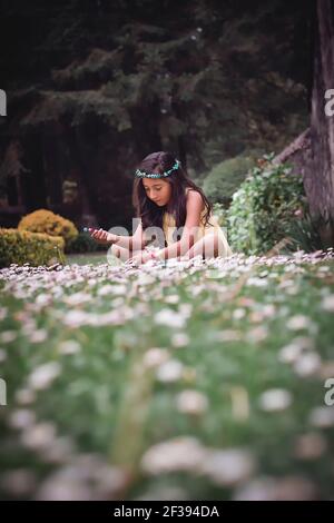 Adolescente assise sur l'herbe dans un parc portant une robe hippie jaune et une couronne de fleurs Banque D'Images