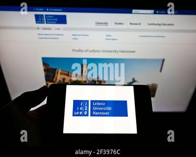 Personne tenant un smartphone avec le logo de l'allemand Gottfried Wilhelm Leibniz Universität Hannover à l'écran devant le site. Mise au point sur l'affichage du téléphone. Banque D'Images