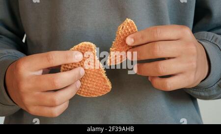 Jeune homme tenant deux moitiés Dutch caramel gaufré traditionnel fait à la main fond de sweat-shirt gris dessert Banque D'Images