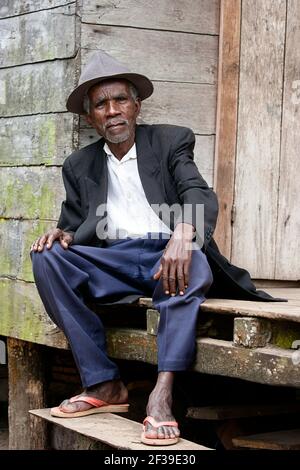 Portrait d'un vieil homme malgache joliment habillé pour les vacances de Famadihana portant un chapeau assis devant une maison dans un village près de Maroansetra, Madagascar Banque D'Images