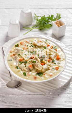poisson poché dans une sauce à base de lait avec légumes, épices et herbes dans un bol blanc sur une table en bois, vue verticale, cuisine anglaise Banque D'Images