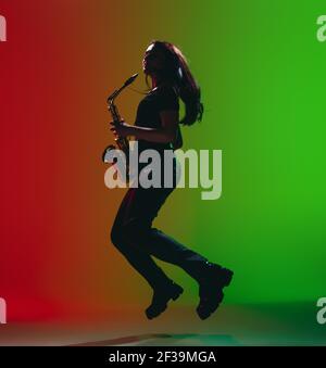 Silhouette de jeune fille avec saxophone posé isolé sur fond vert-rouge. Banque D'Images